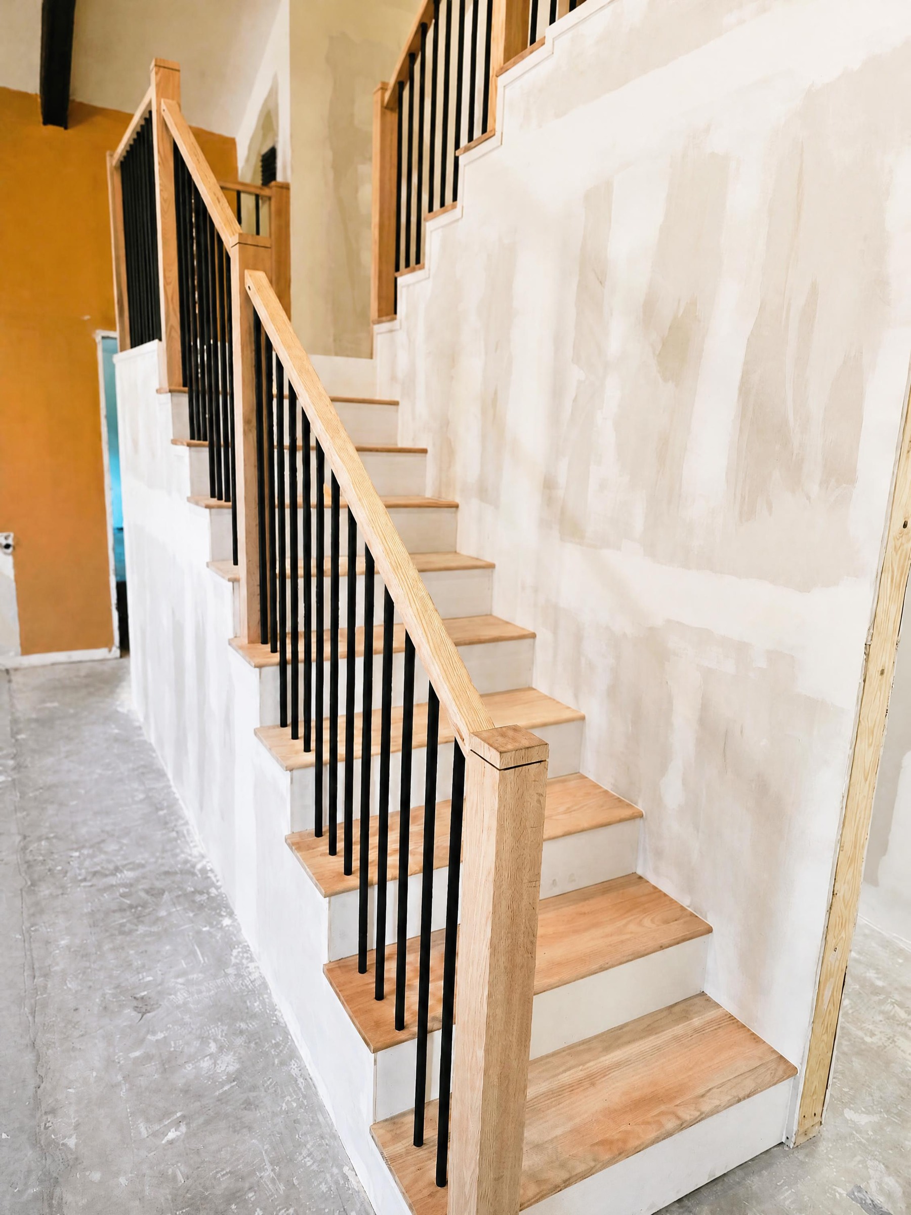 New oak staircase with white risers and black metal balusters installed in an unfinished remodel by Xemplar Construction